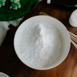 Top view of flour in a bowl with baking utensils on a wooden table, ready for preparation.